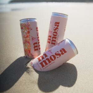 Three pink cans of beverage sitting in the sand at a beach
