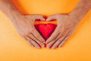 Heart Inside A Man's Hands On Orange Background, Top View.